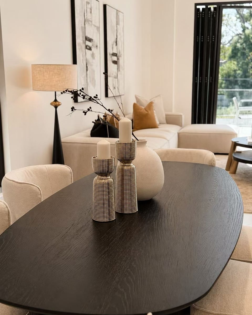 Black oval dining table with ribbed vases in front of a cream sofa, a floor lamp and two framed black and white artworks