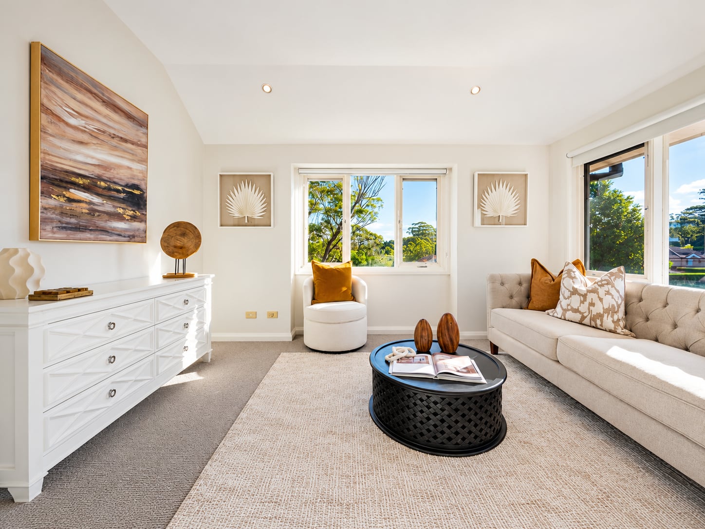 Upstairs sitting room with a tufted cream sofa, a black carved coffee table, a white dresser and windows to the trees