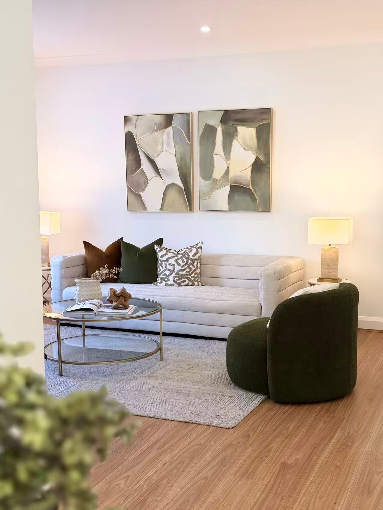 Living room with a channelled cream sofa, a green bouclé armchair, a round glass coffee table and two framed abstract artworks