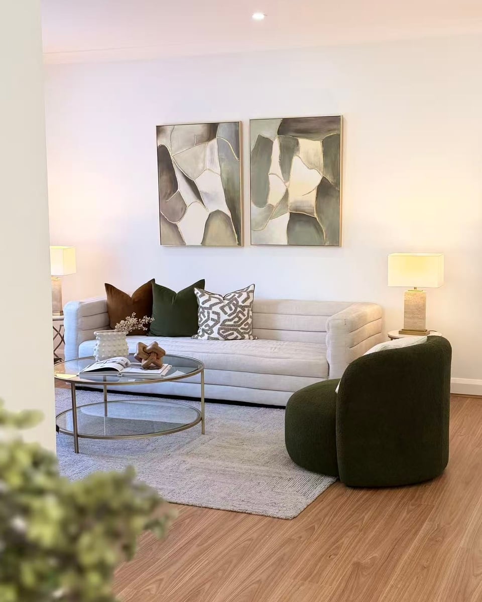 Living room with a channelled cream sofa, a green bouclé armchair, a round glass coffee table and two framed abstract artworks