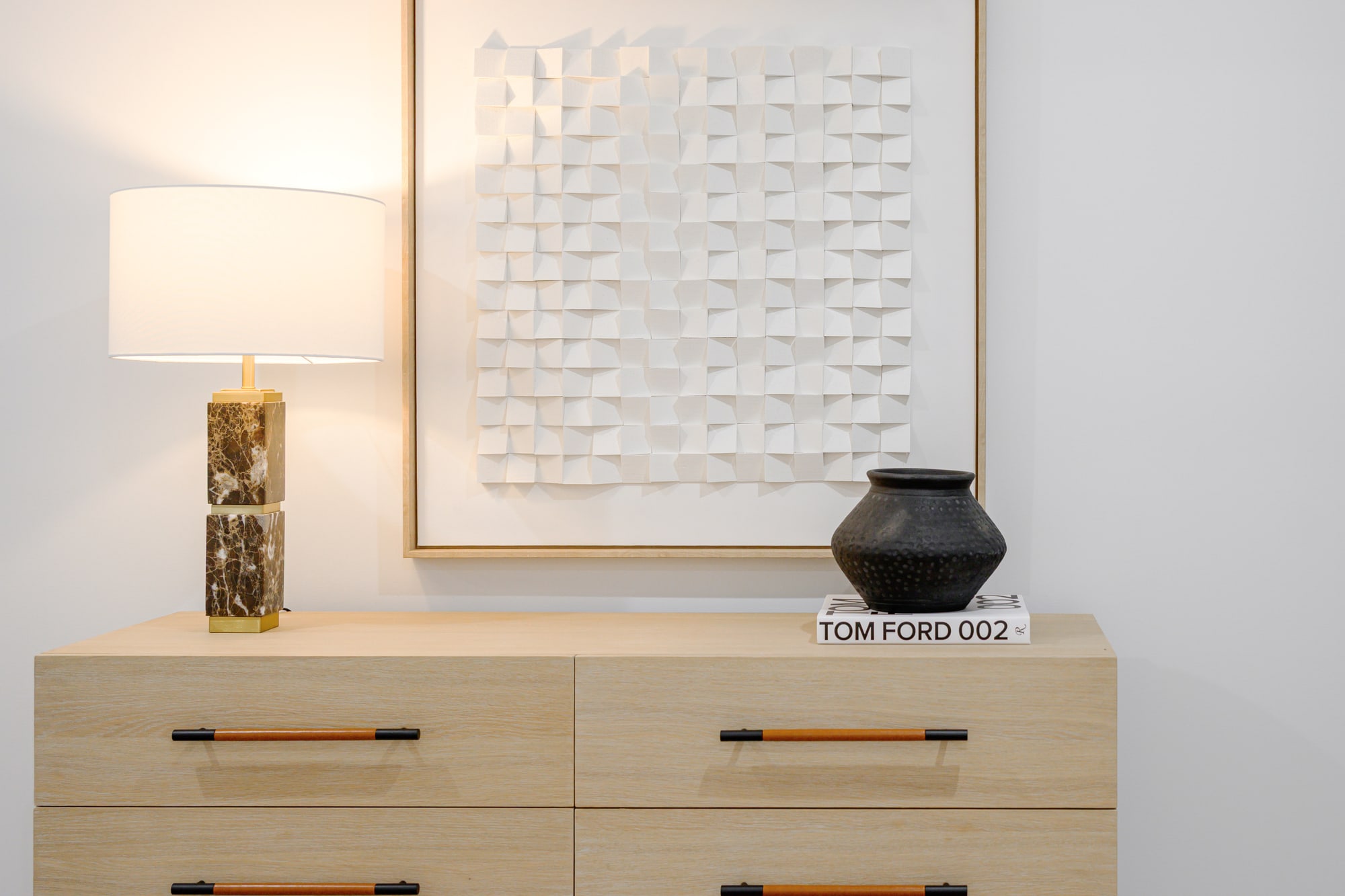 Pale timber entry console styled with a table lamp, a framed textured artwork and a black vase