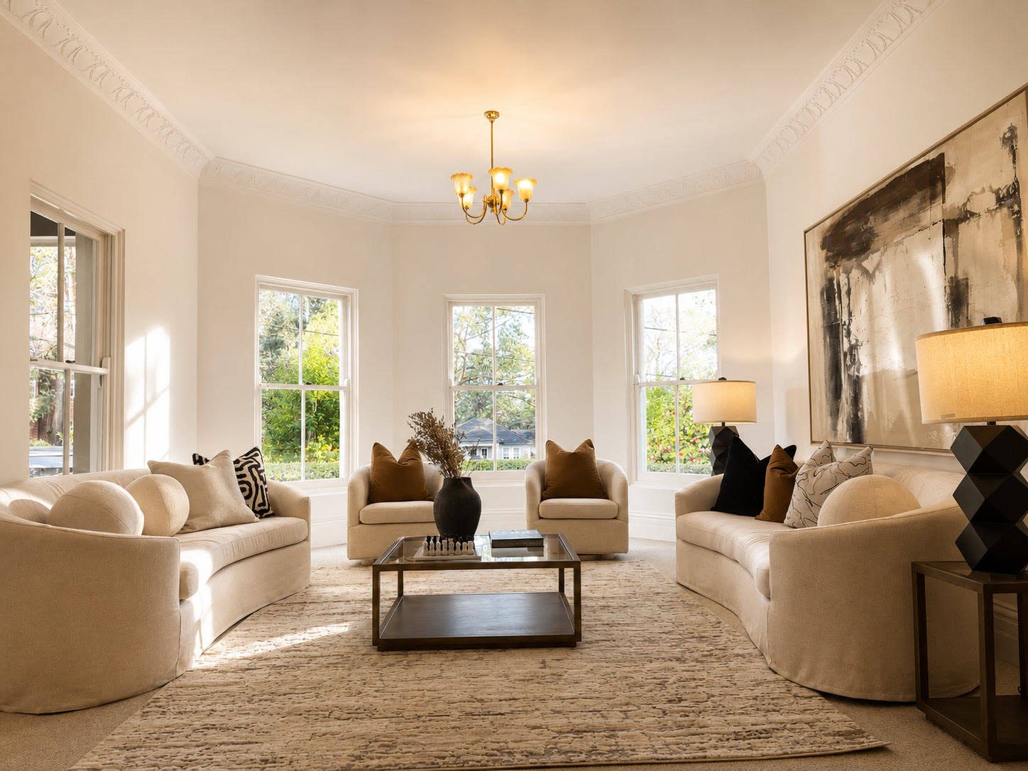 Formal living room with curved cream sofas, a large abstract painting, bay windows and a brass chandelier