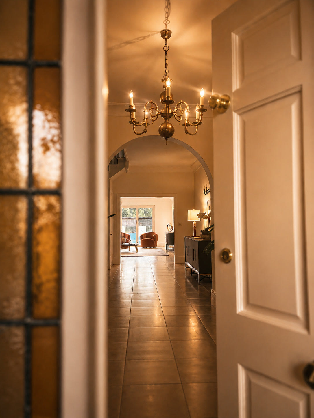 Warmly lit hallway with a chandelier, an arched opening and a panelled door