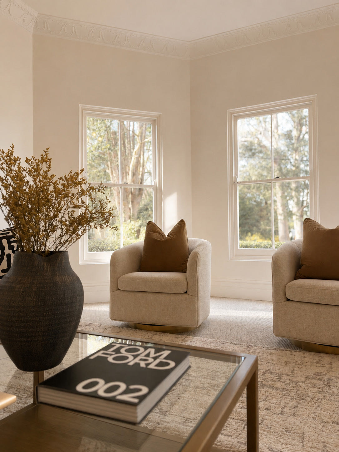 Sitting room corner with cream swivel armchairs, a glass coffee table and tall windows