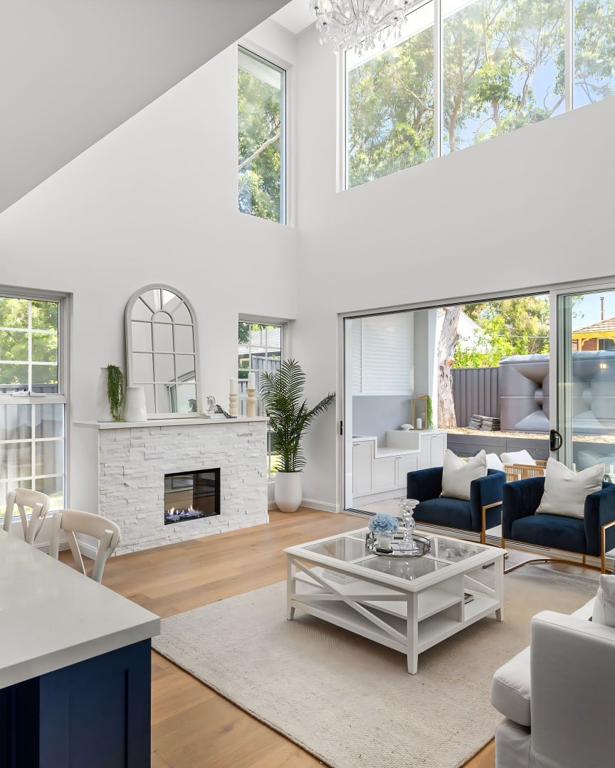 Miranda open-plan living area with navy armchairs, a white sofa and a stone fireplace beside the kitchen
