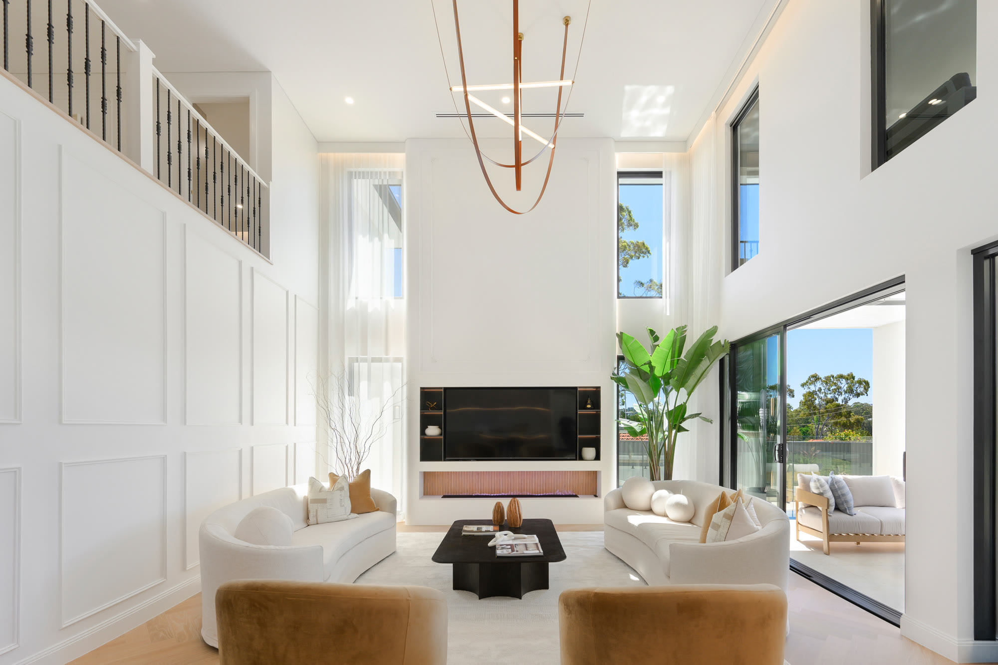 Styled double-height living room with curved cream sofas, mustard velvet chairs and a black coffee table in front of a panelled wall