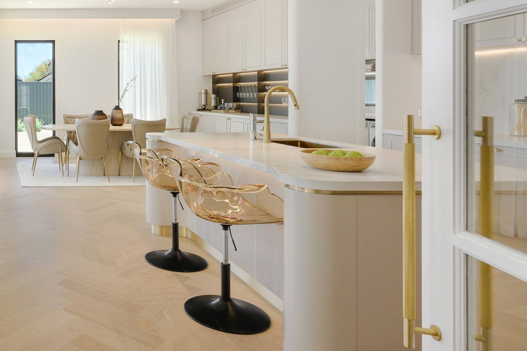 Kitchen island with gold-footed bar stools and a curved tan armchair in the open-plan living area