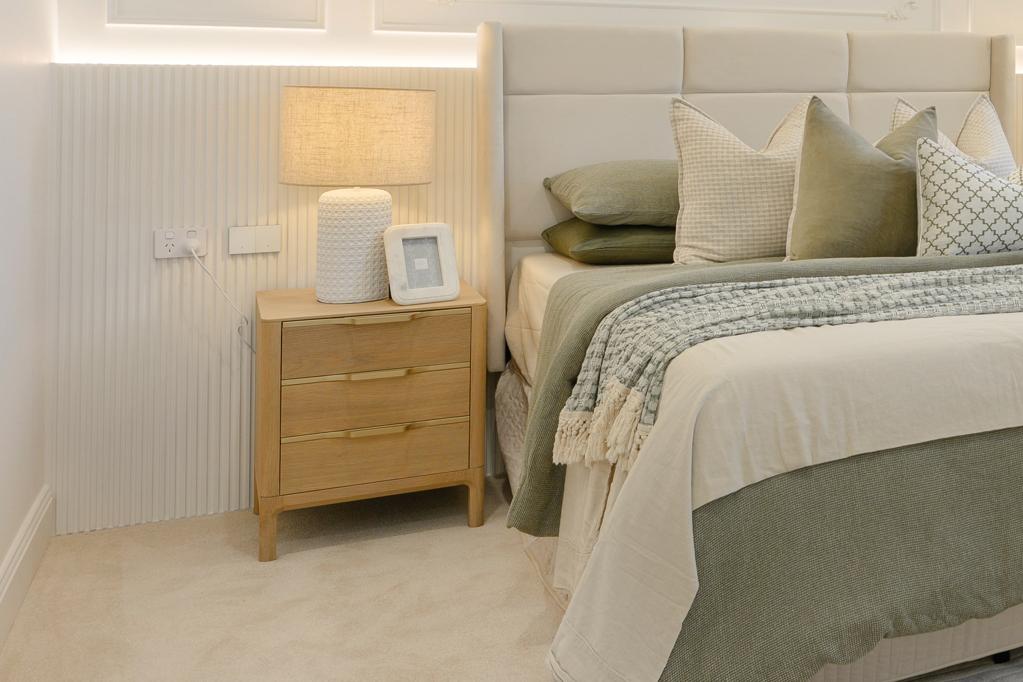 Bedside table with a lamp beside a sage green and cream bed