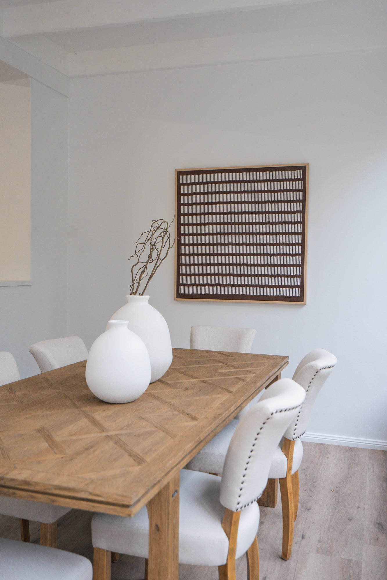 Sunroom dining area with a timber table, cream studded dining chairs and a framed striped artwork