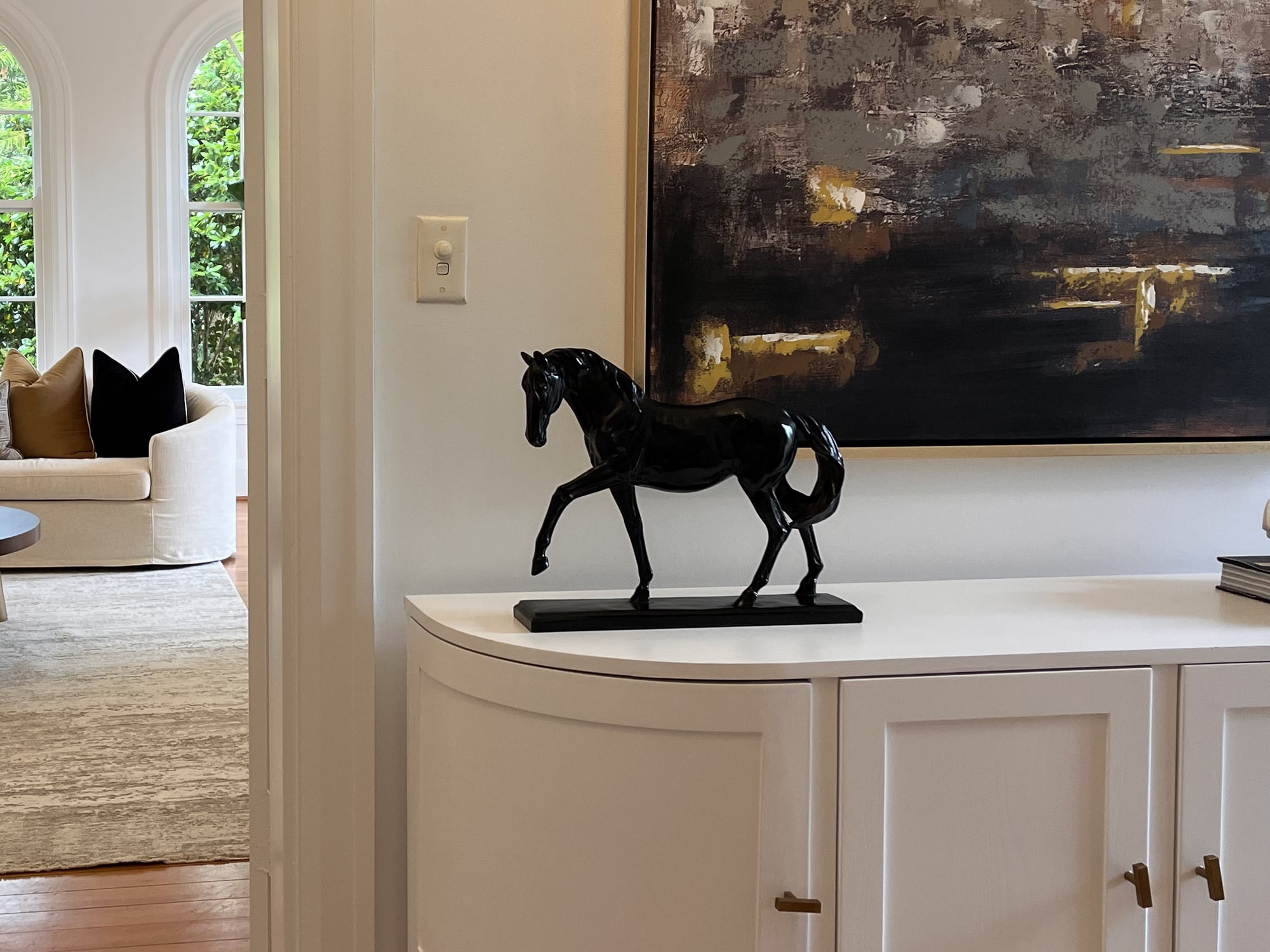 Black horse sculpture on a white cabinet beneath a large abstract painting