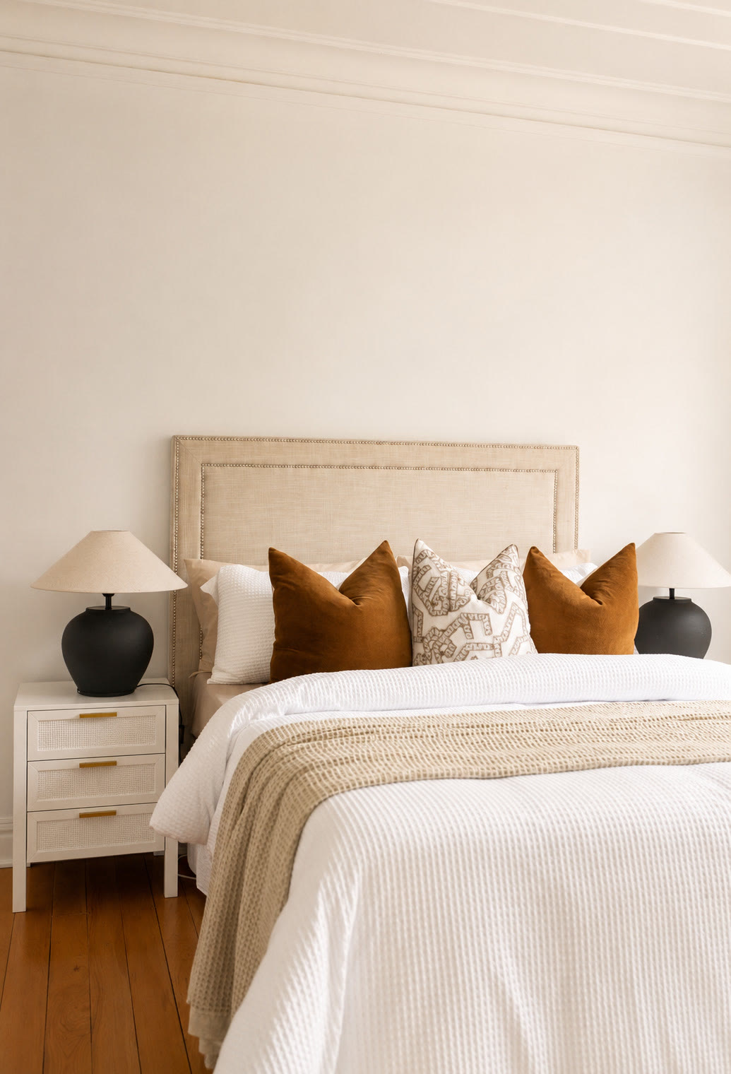 Bedroom with a linen bedhead, rust cushions and a cream knitted throw