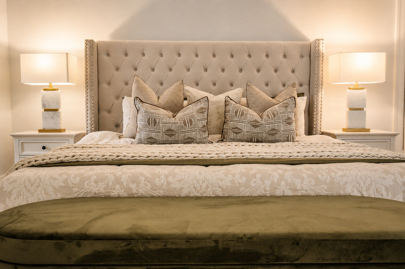 Bed with a tufted bedhead, gold lamps and an olive green velvet bench