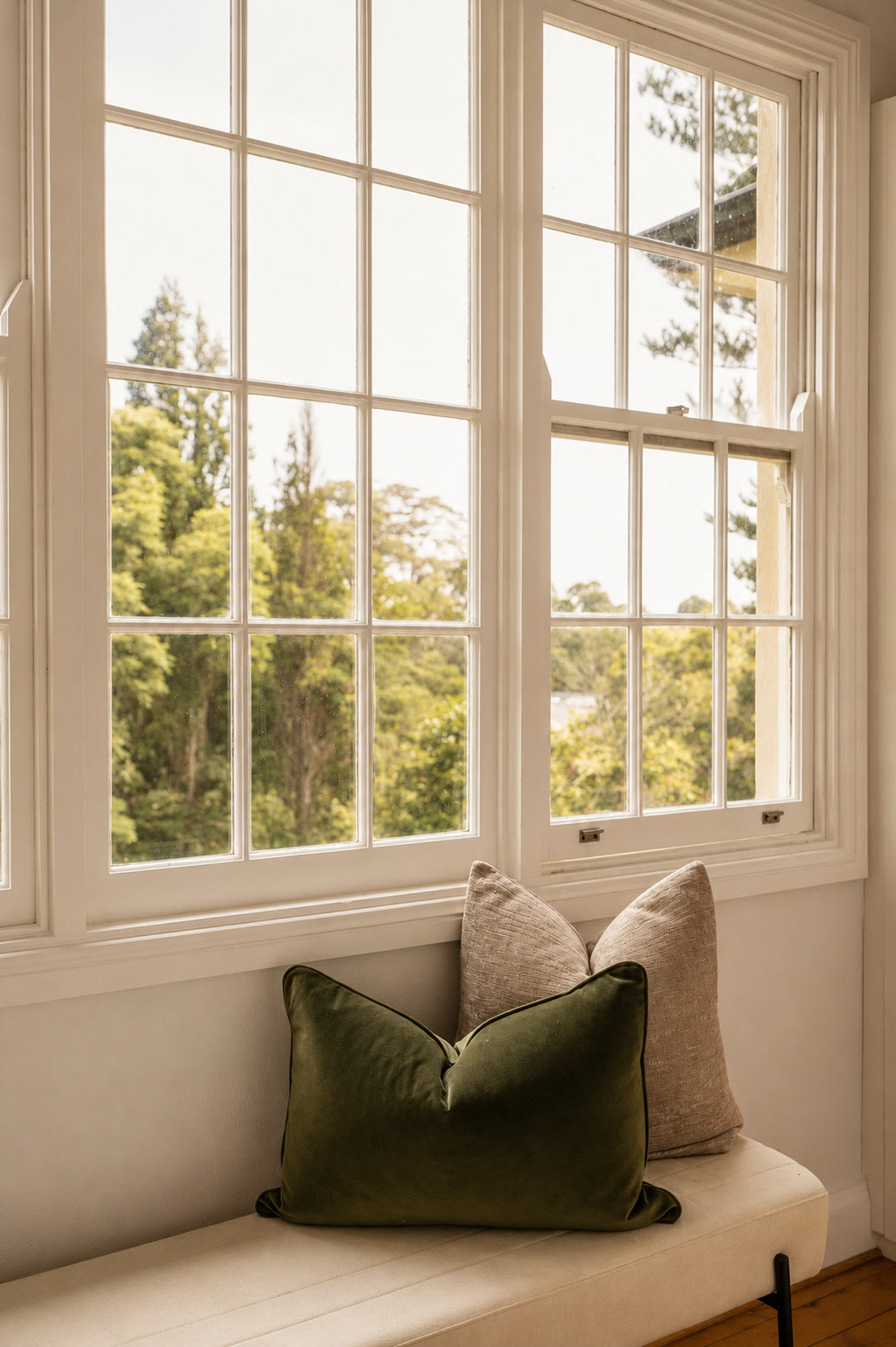 Window seat with an olive green cushion beside a multi-pane window