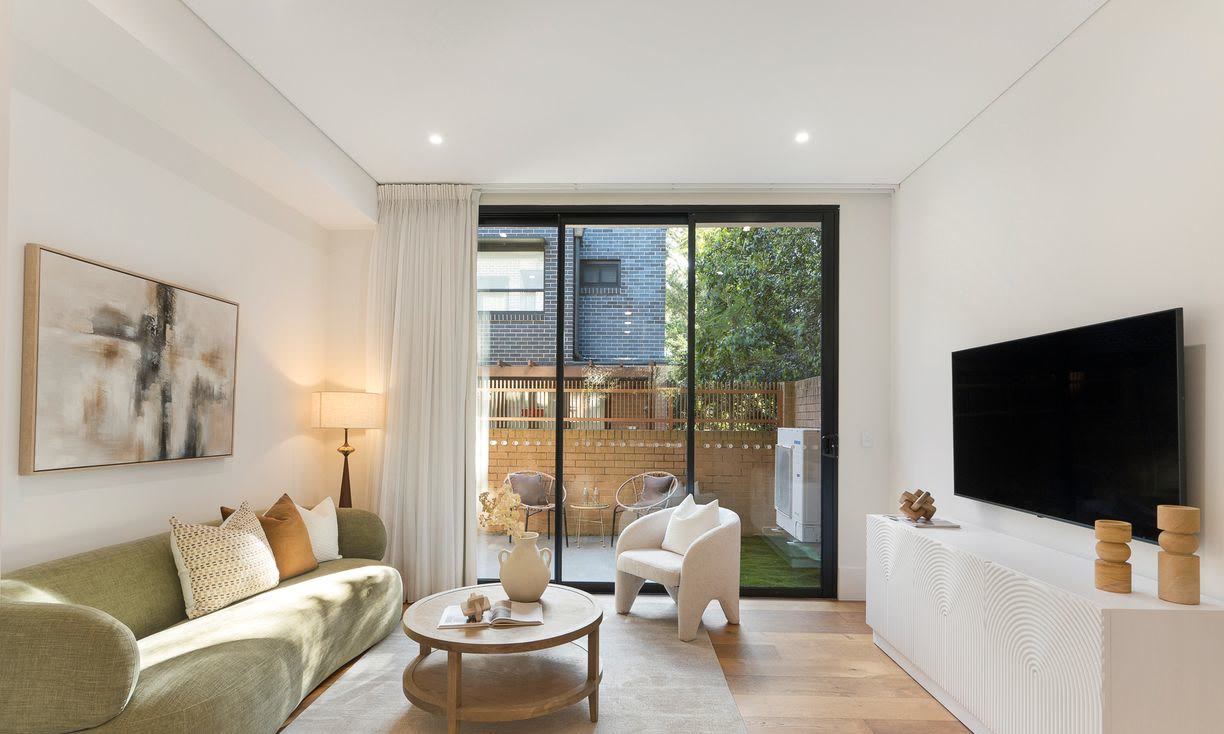 Living room with a curved green sofa, a round timber coffee table, a wall-mounted television and glass doors to a courtyard