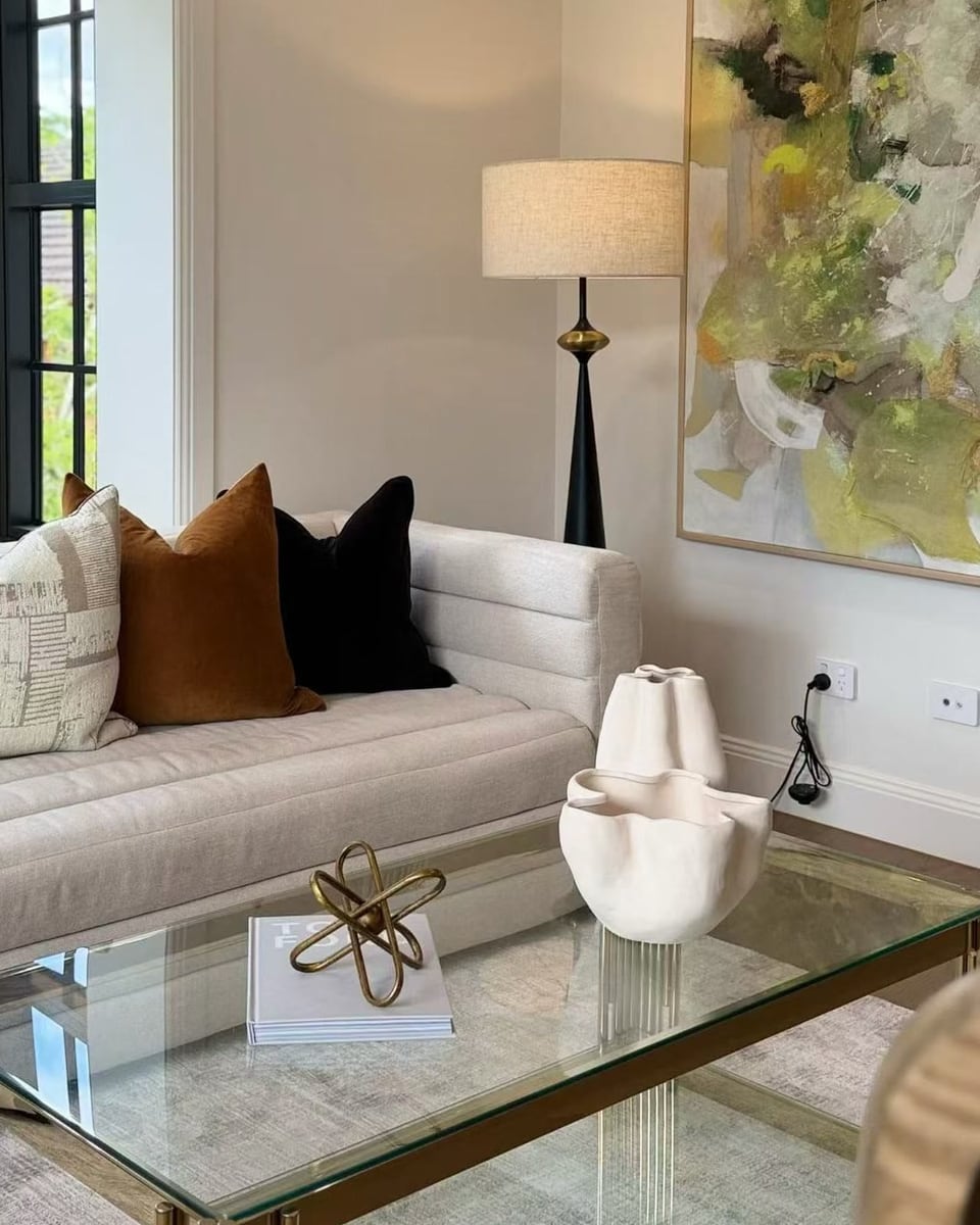 Cream sofa cushions beside a glass coffee table styled with a sculpture and books