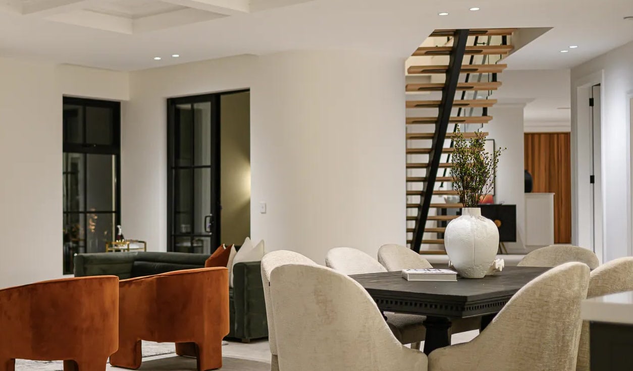 Floating timber staircase beside a dining table with cream chairs