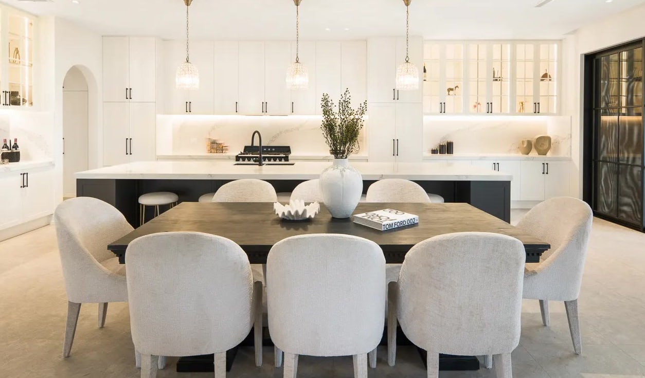 Long dining table with round-backed cream chairs in front of an open kitchen