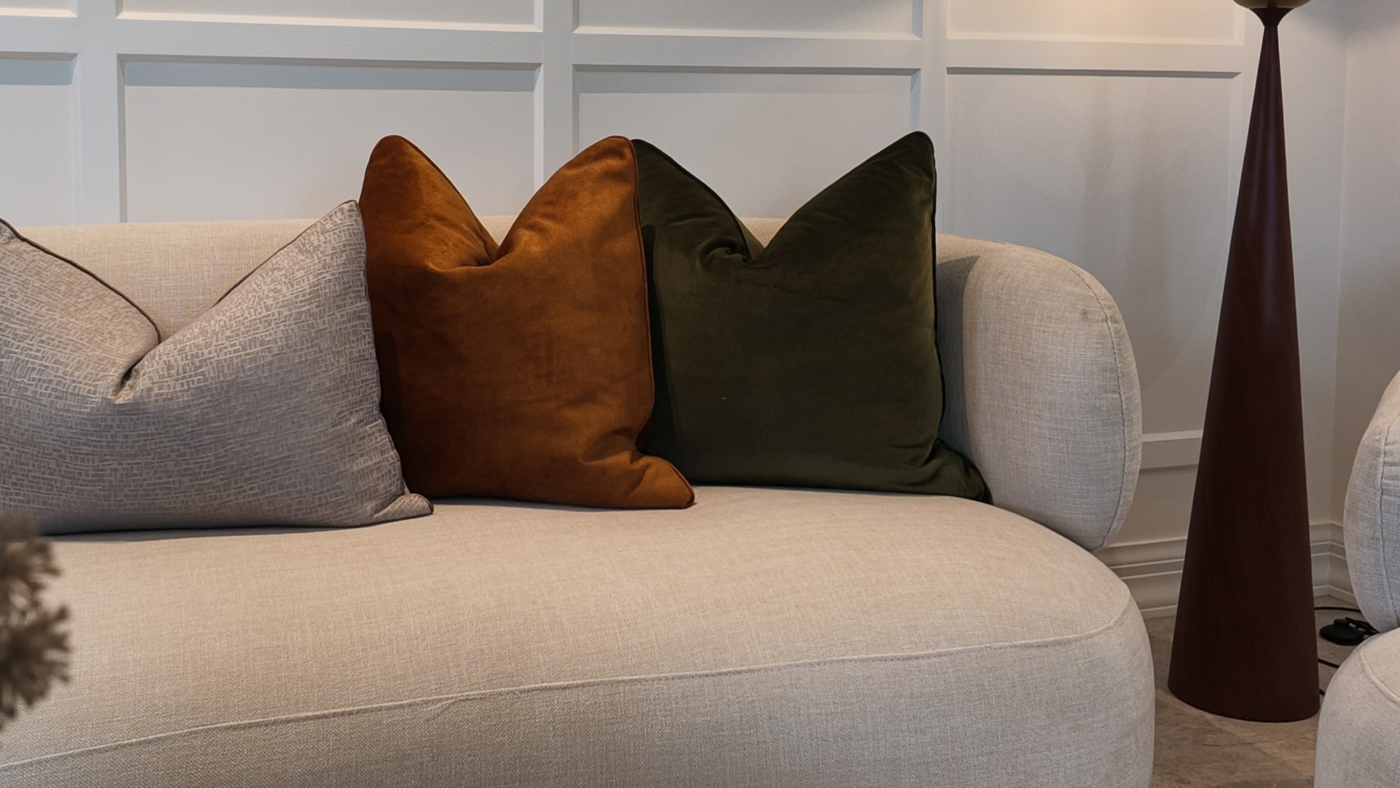 Curved cream sofa with rust and green cushions and a tall table lamp