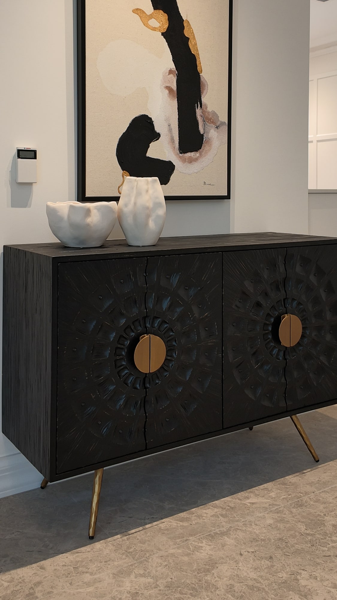 Black carved sideboard with gold handles beneath an abstract painting