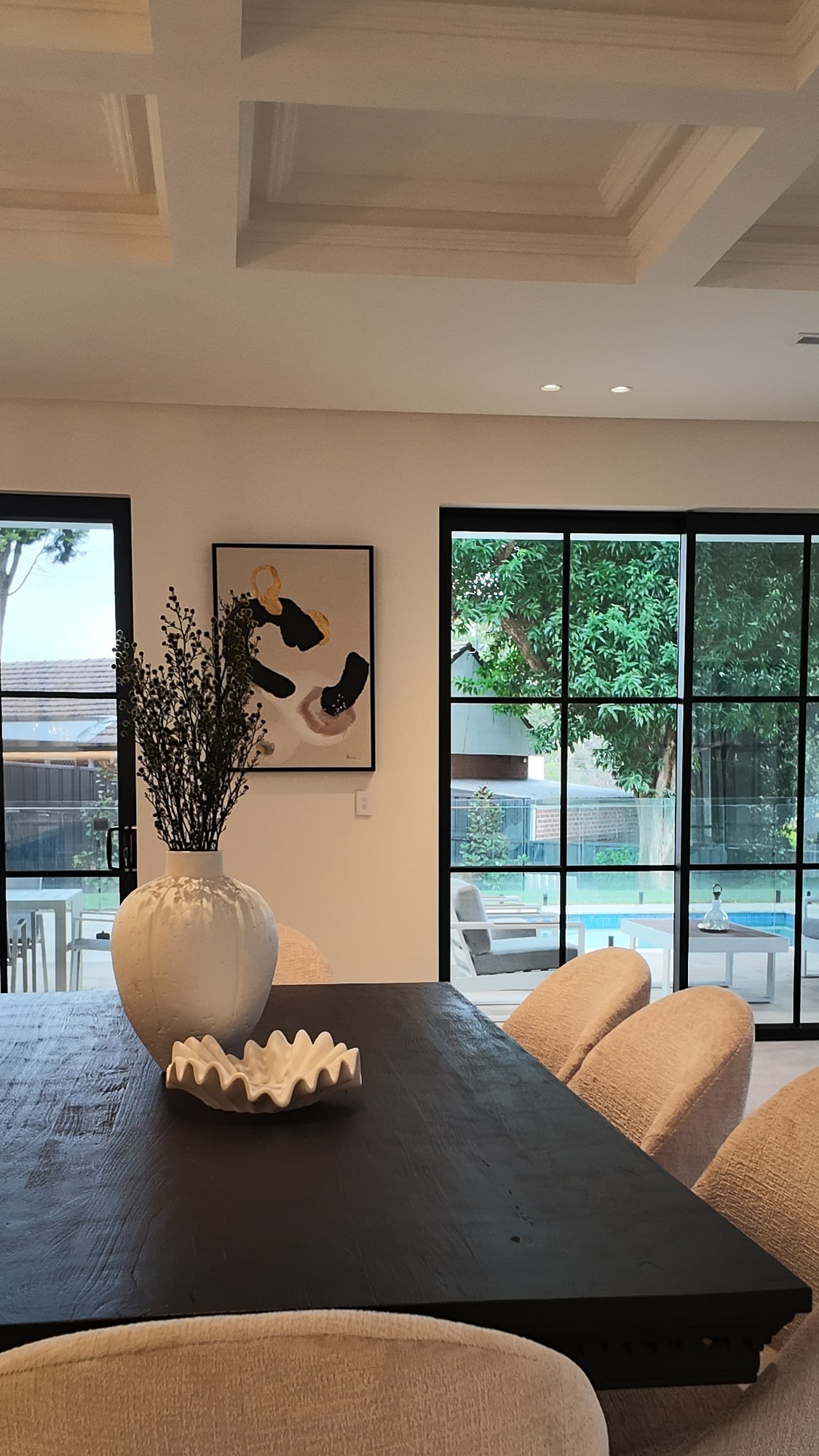 Black dining table styled with a vase of dried branches and a cream upholstered chair