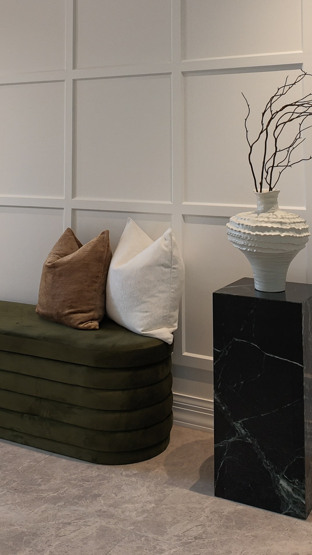 Green velvet bench with a cushion beside a black marble plinth