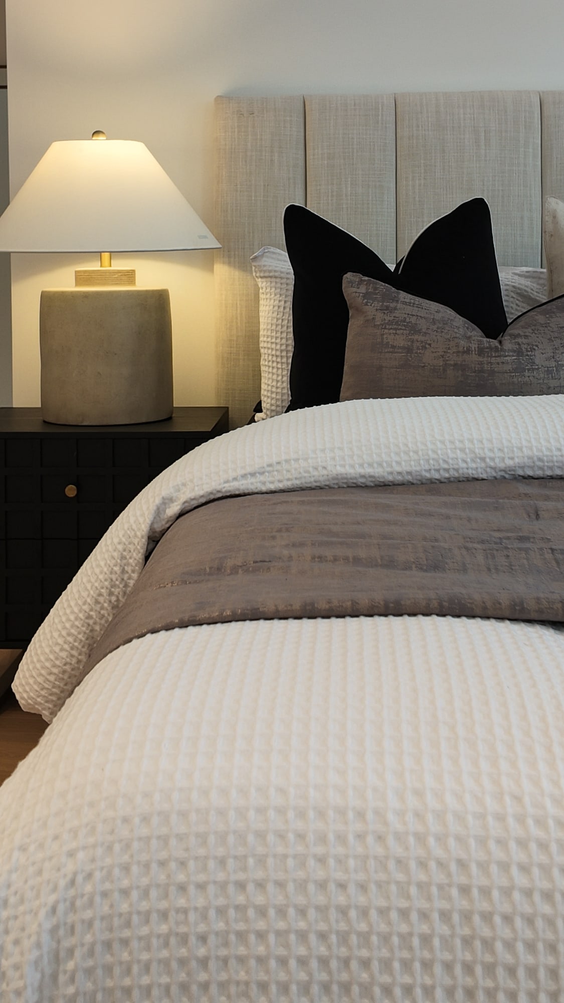 Pale channelled bedhead with black and grey cushions and a table lamp