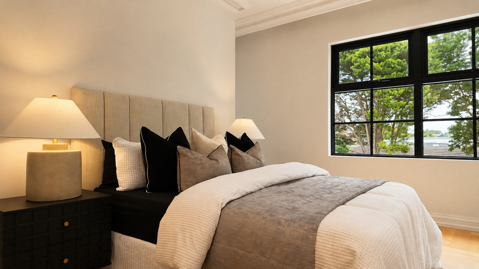 Bedroom with a channelled bedhead, black and grey cushions and a large black-framed window