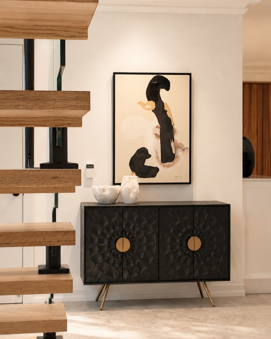Black carved sideboard and abstract painting beside a floating timber staircase
