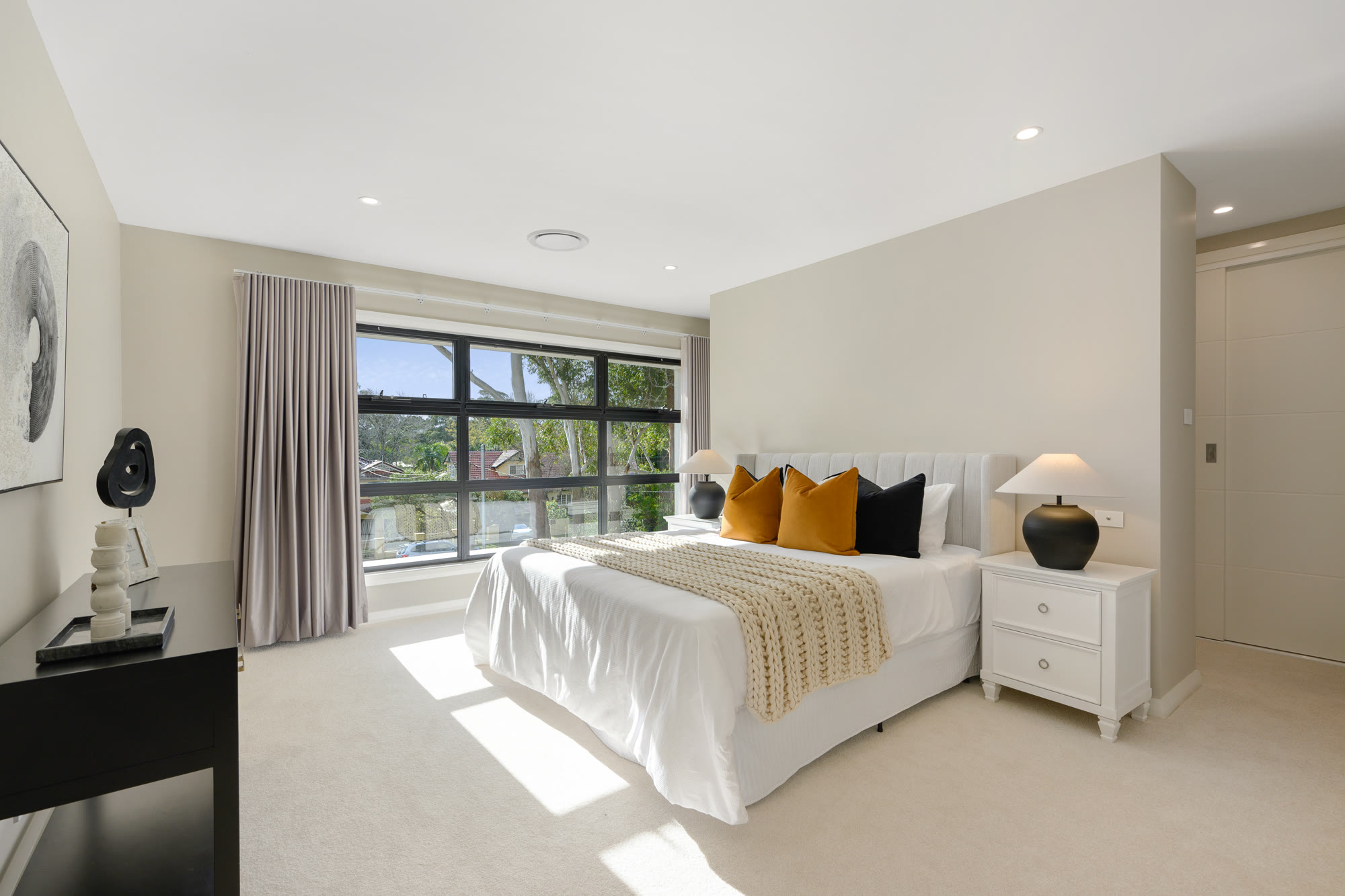 Main bedroom styled with white bedding, mustard and black cushions, a knitted throw and a black table lamp
