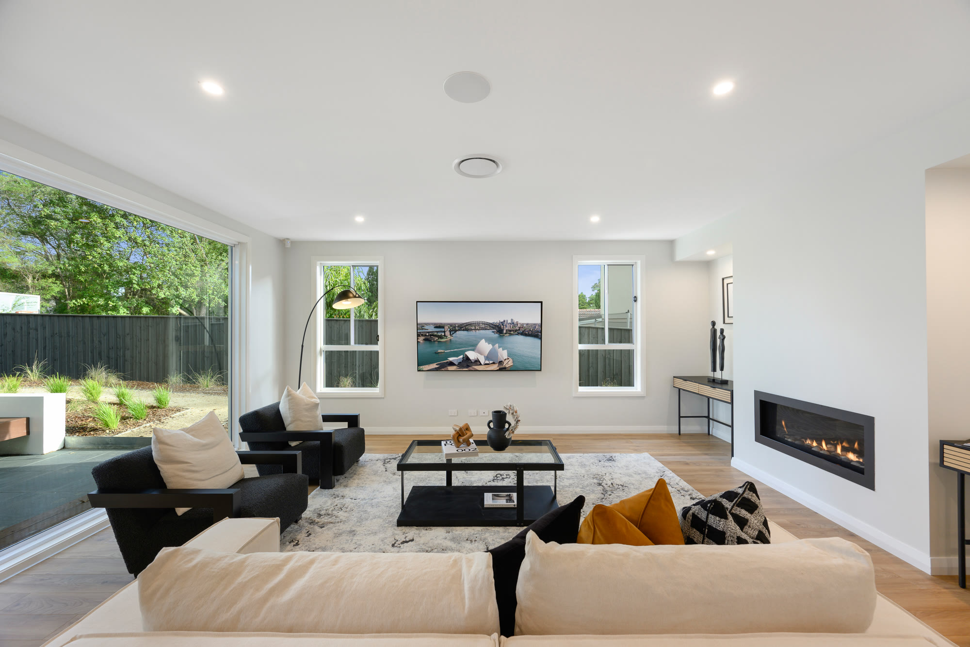 Living room with a cream modular sofa, black armchairs, a linear fireplace and a glass coffee table, opening to the garden