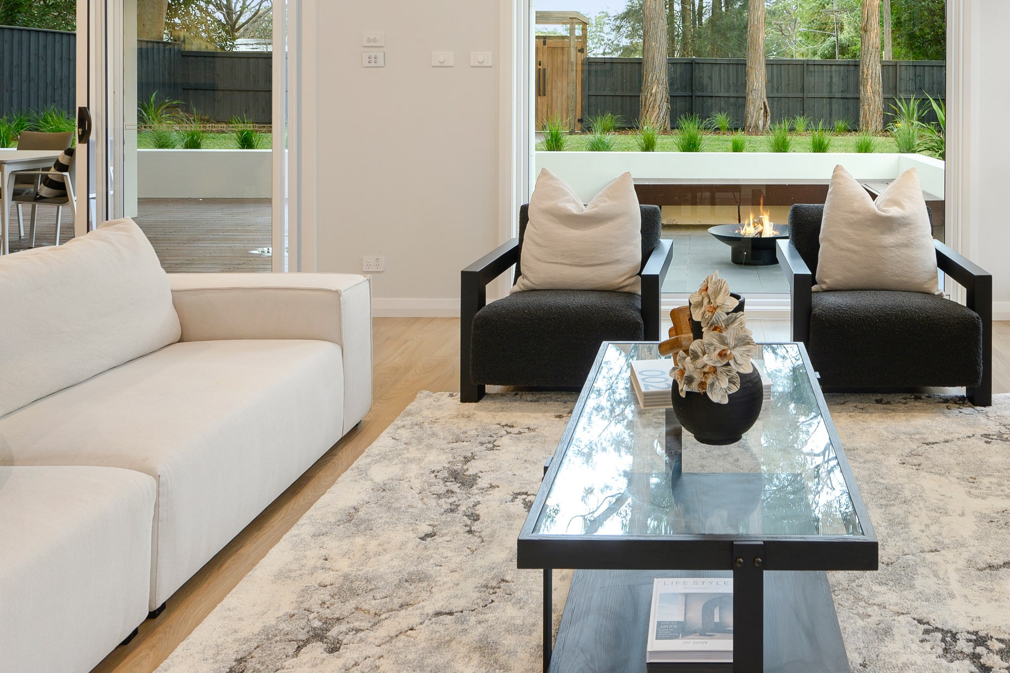 Cream sofa with mustard and black cushions beside a black glass coffee table on a patterned rug