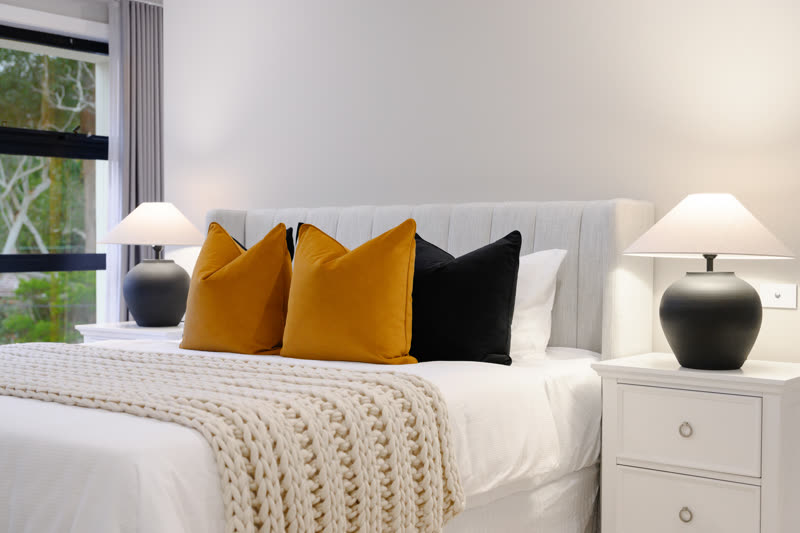 Bedhead detail with mustard and black cushions, a knitted throw and a pair of black table lamps