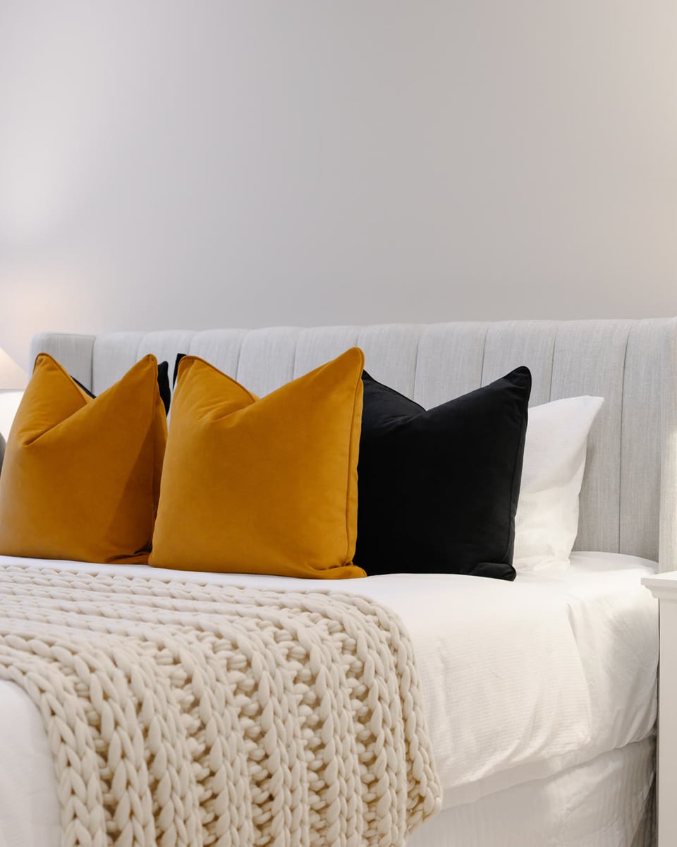 Bedhead detail with mustard and black cushions, a knitted throw and a pair of black table lamps